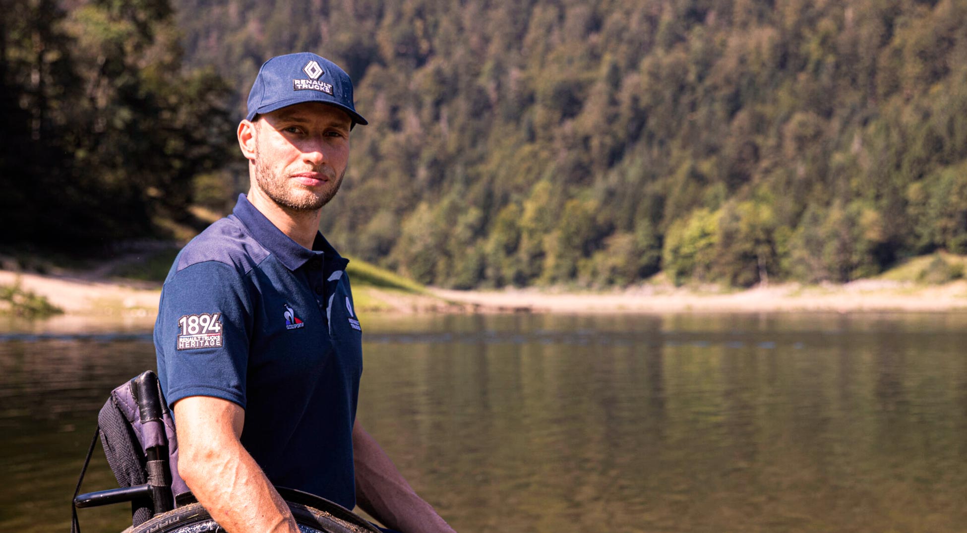 Man wearing Le Coq Sportif cap and t-shirt. By a lake. 