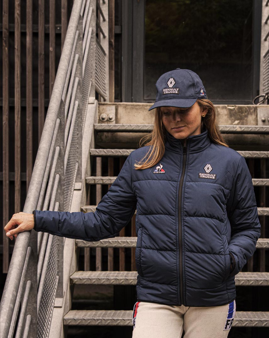 Woman wearing jacket and cap with Le Coq Sportif. Outdoor in a staircase.